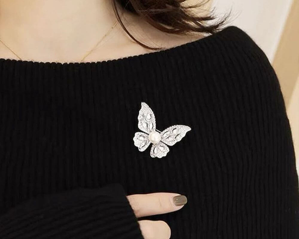 Chic butterfly-shaped brooch with dazzling crystals and a pearl, styled on a black cotton sweater