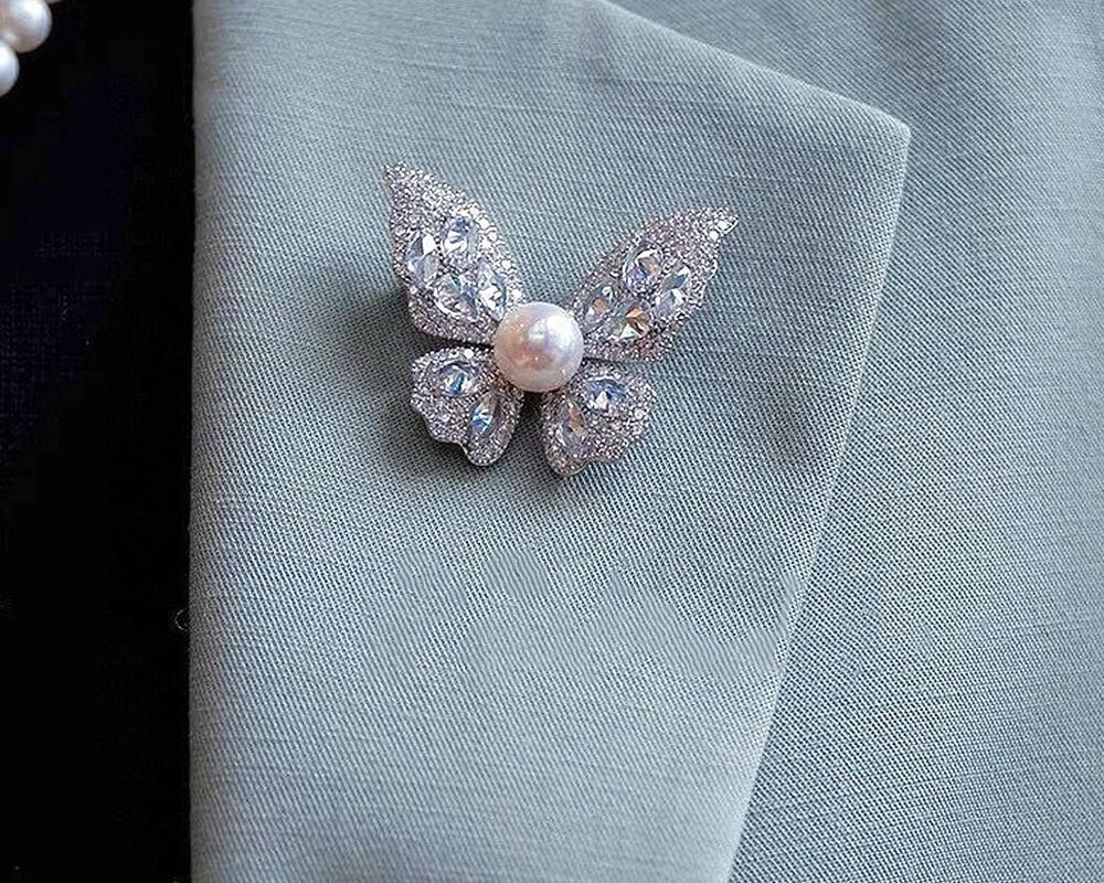 Sophisticated butterfly brooch adorned with sparkling crystals and a pearl centerpiece, pinned to a soft fabric