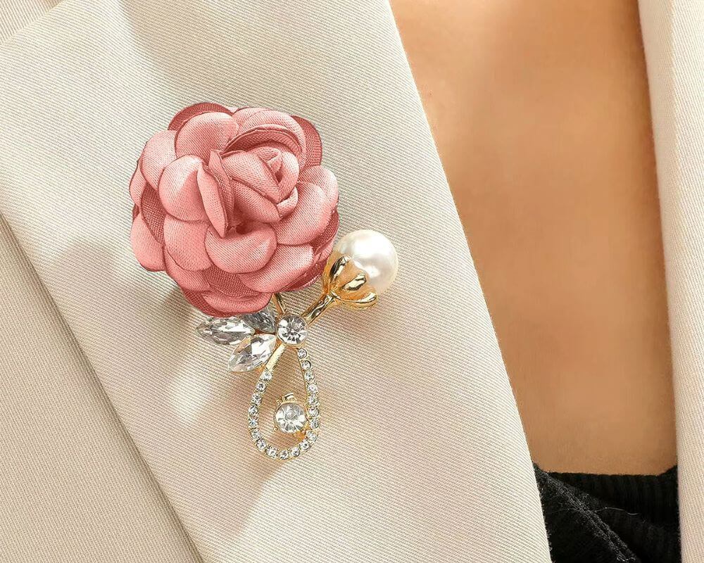 Beautiful brooch featuring a pink satin rose, gold accents, and crystal embellishments, styled on a beige lapel